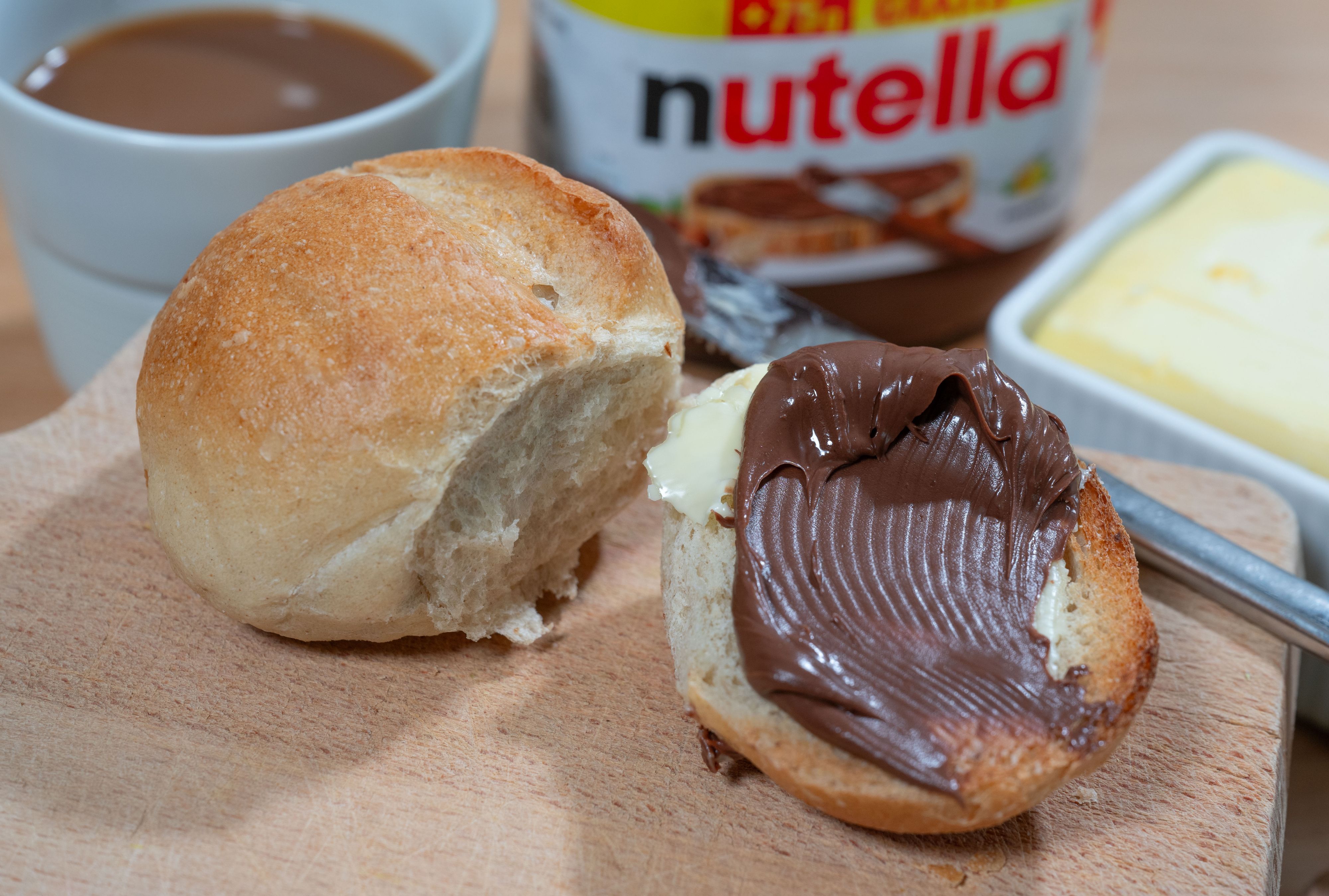 Brötchen mit Nuss-Nougat-Aufstrich und Nutella-Glas im Hintergrund.
