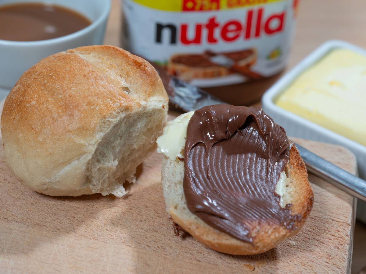Brötchen mit Nuss-Nougat-Aufstrich und Nutella-Glas im Hintergrund.