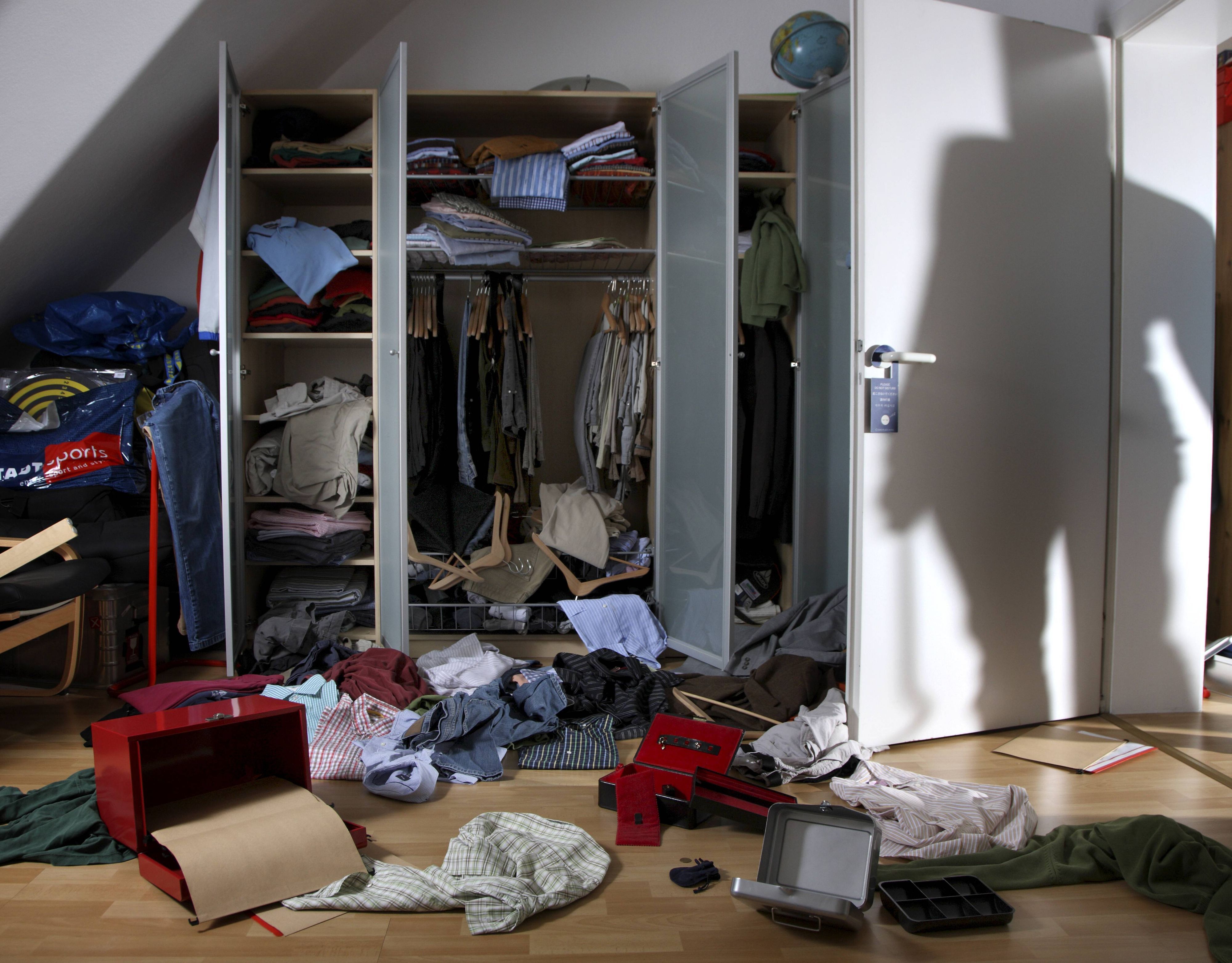 Kleidung und Schachteln wurde aus einem Schrank gerissen und auf den Fußboden geworfen, auf der Zimmertür ist der Schatten eines Einbrechers zu sehen.