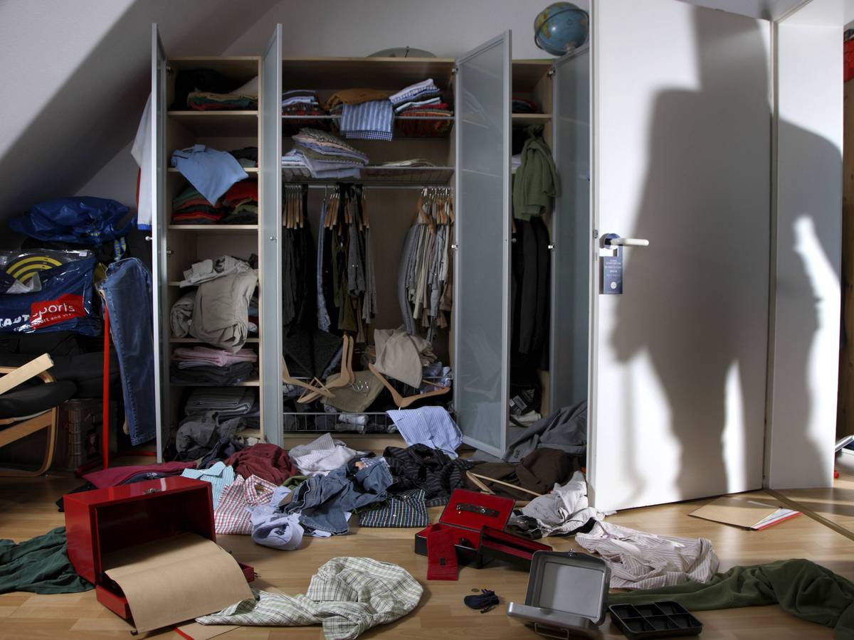 Kleidung und Schachteln wurde aus einem Schrank gerissen und auf den Fußboden geworfen, auf der Zimmertür ist der Schatten eines Einbrechers zu sehen.