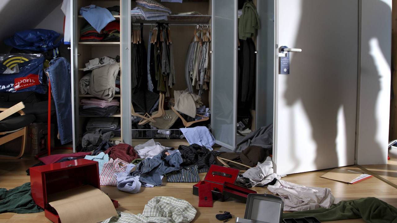 Kleidung und Schachteln wurde aus einem Schrank gerissen und auf den Fußboden geworfen, auf der Zimmertür ist der Schatten eines Einbrechers zu sehen.