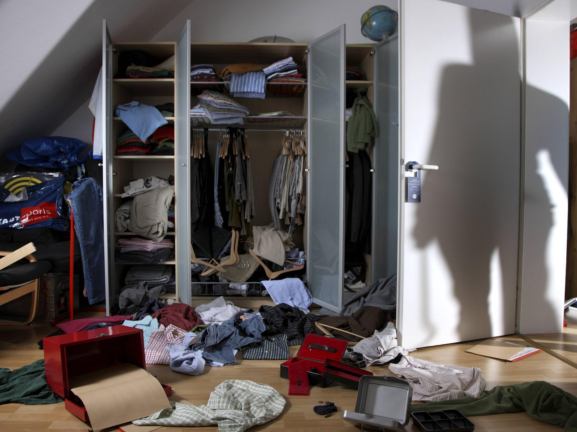 Kleidung und Schachteln wurde aus einem Schrank gerissen und auf den Fußboden geworfen, auf der Zimmertür ist der Schatten eines Einbrechers zu sehen.