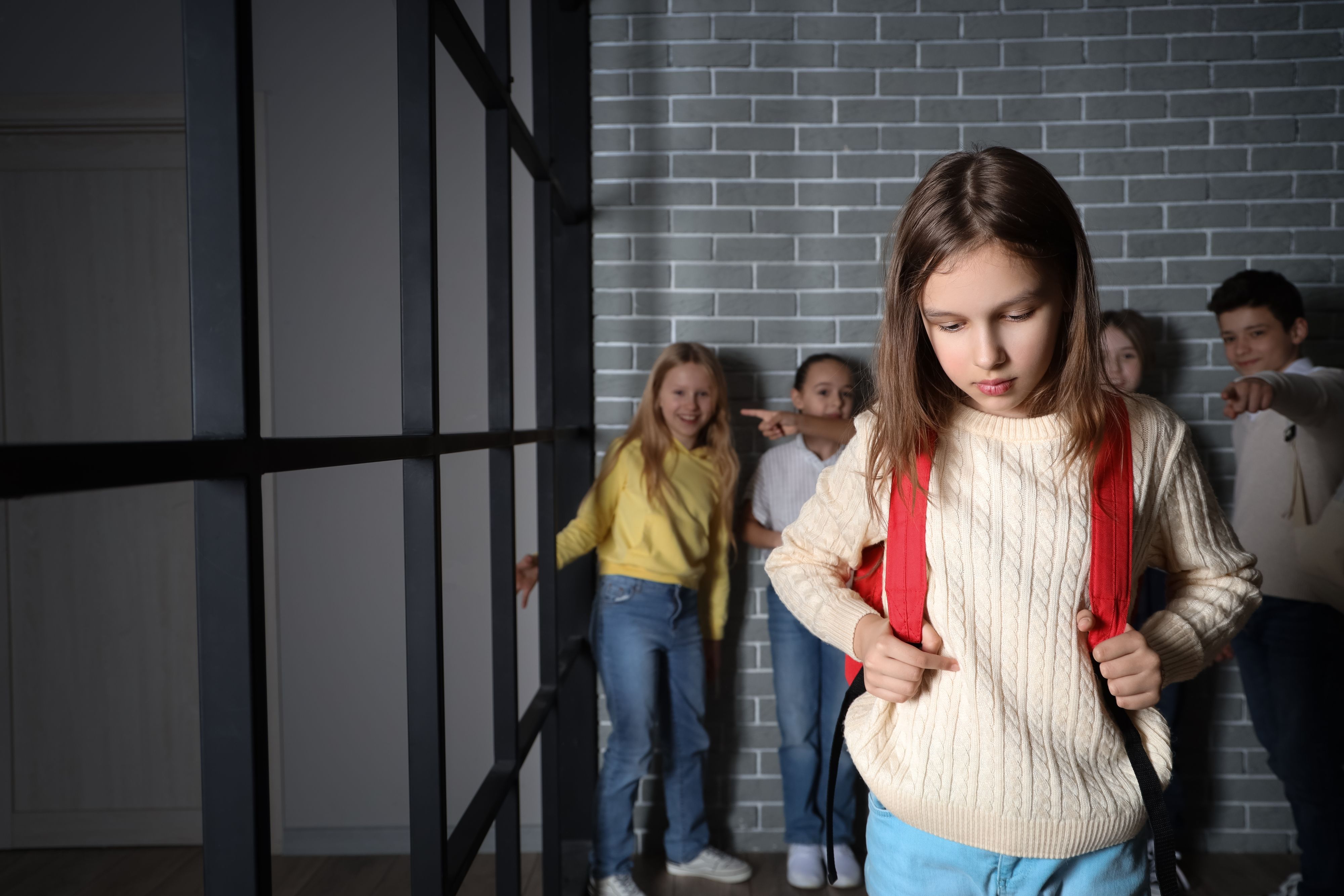 Kinder lachen ein trauriges Mädchen aus und zeigen mit den Kindern auf das Kind