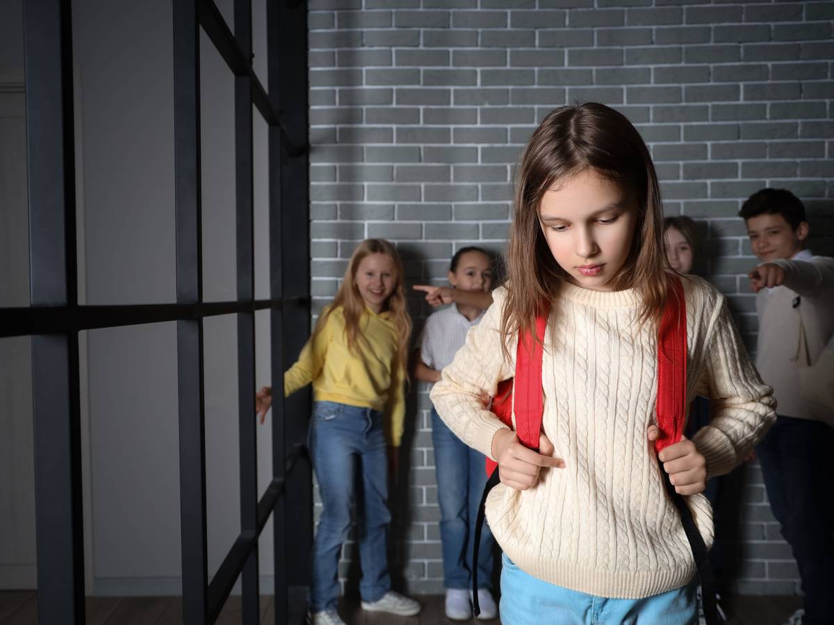 Kinder lachen ein trauriges Mädchen aus und zeigen mit den Kindern auf das Kind