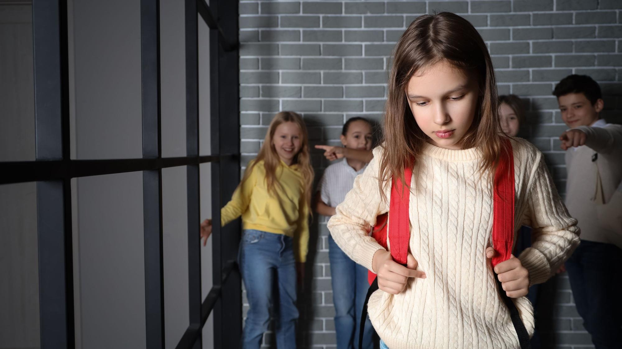 Kinder lachen ein trauriges Mädchen aus und zeigen mit den Kindern auf das Kind