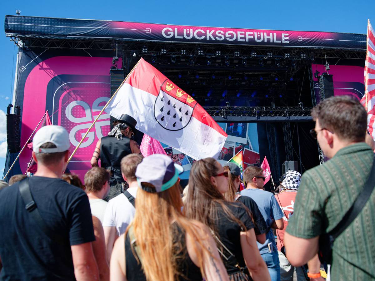 Besucher stehen vor einer Bühne beim Glücksgefühle-Festival auf dem Hockenheimring und halten eine Kölner Stadtflagge. Auch der Kölner Männerchor „Die Gürngürtelrosen“ trat auf dem Hockenheimring auf.