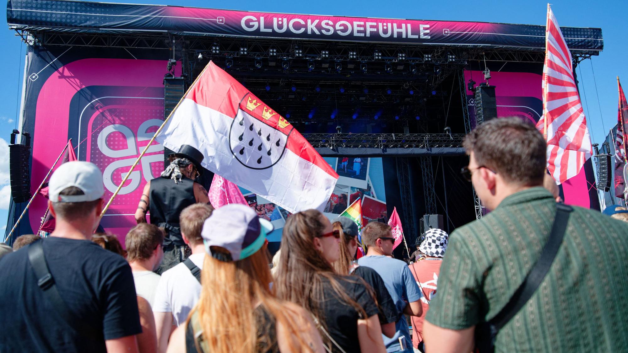 04.09.2026, Baden-Württemberg, Hockenheim: Besucher stehen vor einer Bühne beim Glücksgefühle-Festival auf dem Hockenheimring und halten eine Kölner Stadtflagge. Foto: Uwe Anspach/dpa +++ dpa-Bildfunk +++