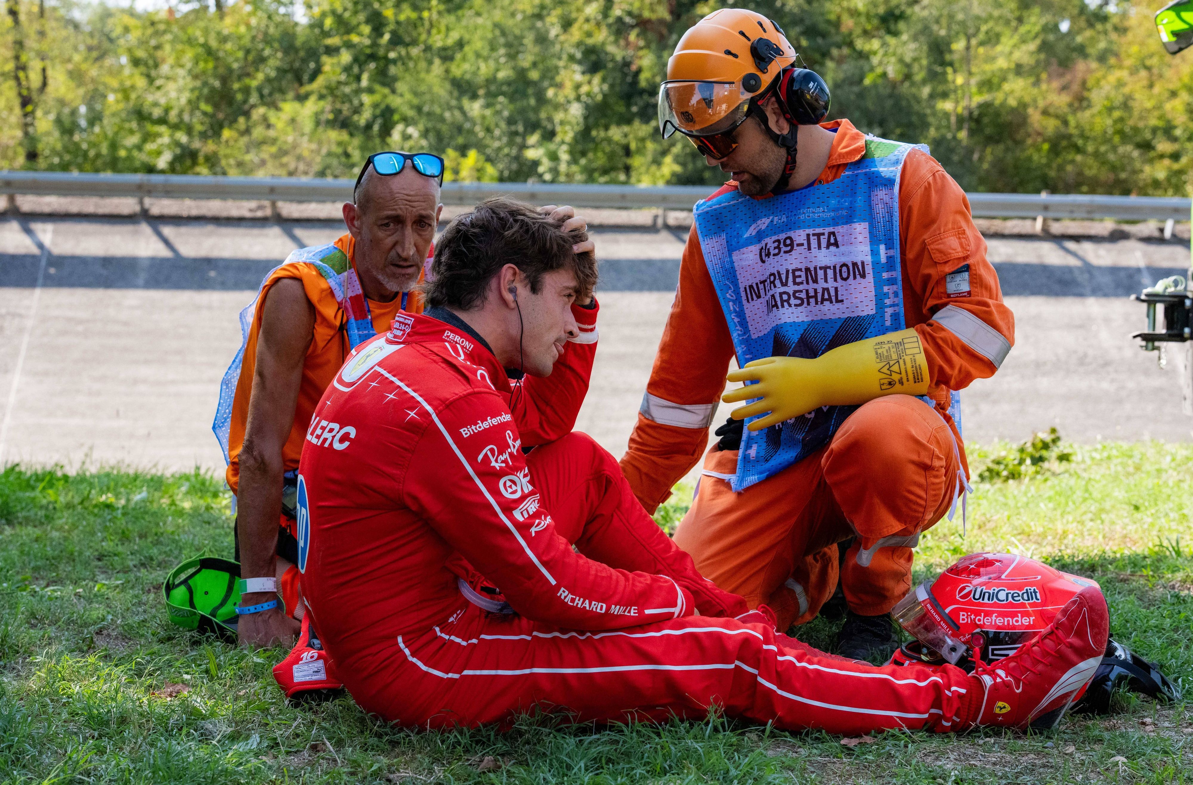 Charles Leclerc sitzt auf dem Rasen, Betreuer sind bei ihm.