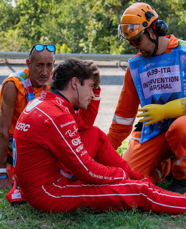 Charles Leclerc sitzt auf dem Rasen, Betreuer sind bei ihm.