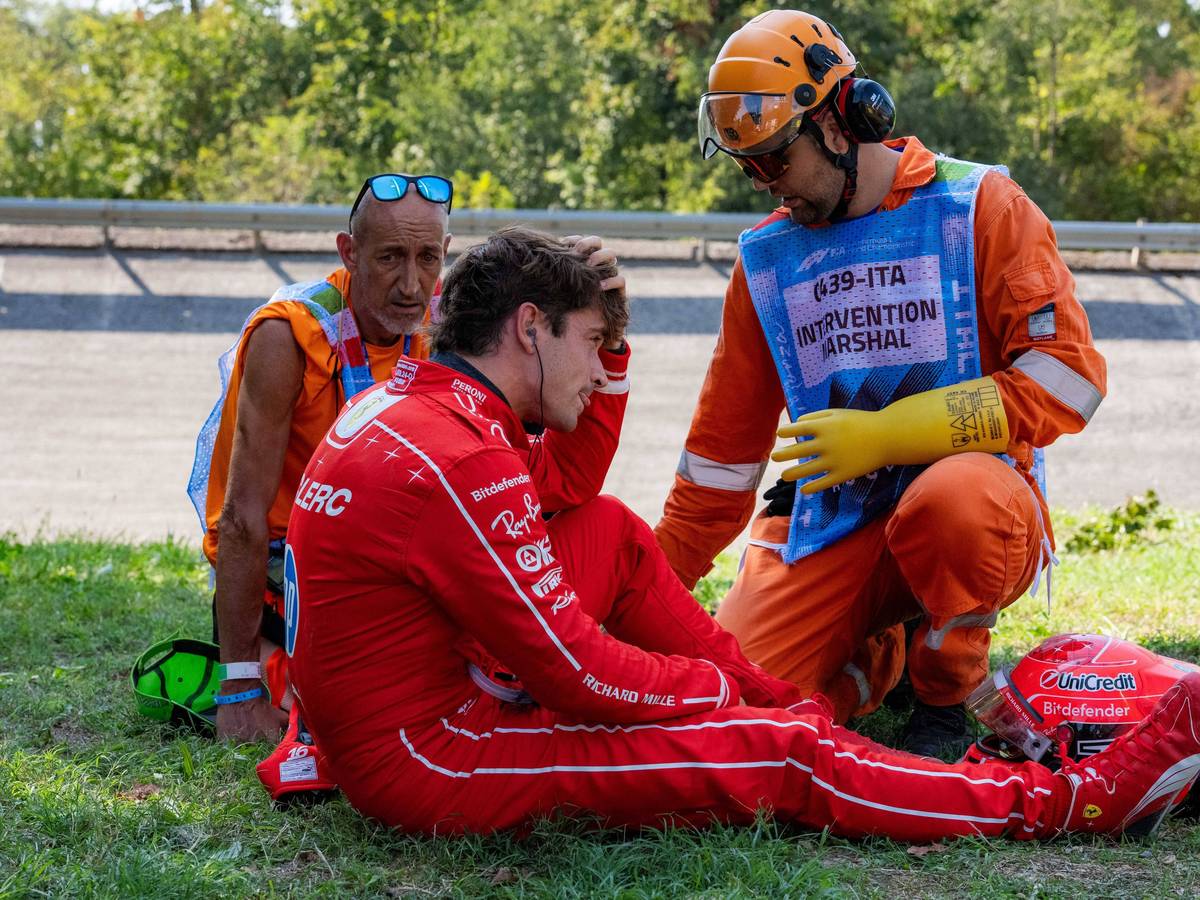 Charles Leclerc sitzt auf dem Rasen, Betreuer sind bei ihm.