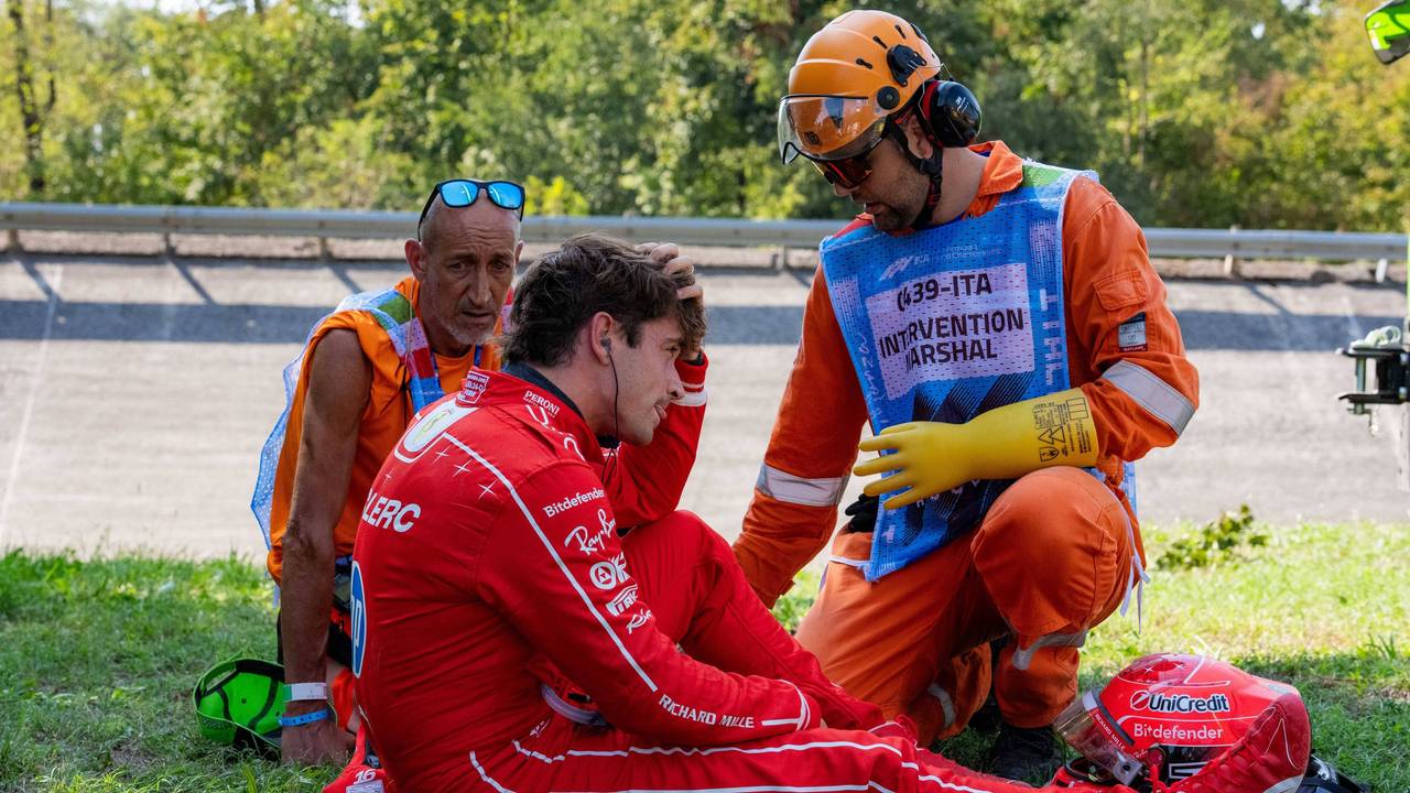 Charles Leclerc sitzt auf dem Rasen, Betreuer sind bei ihm.