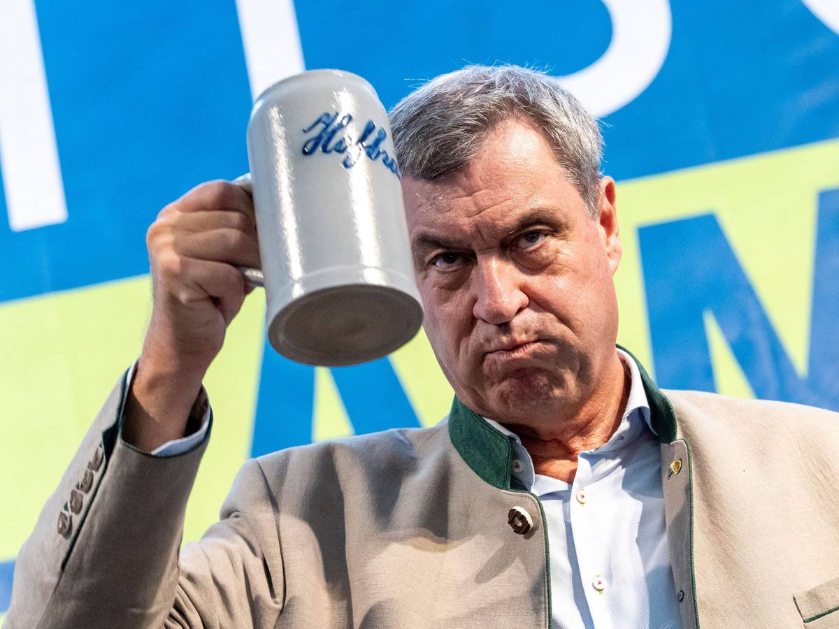 Markus Söder hält ein Getränk in der Hand.