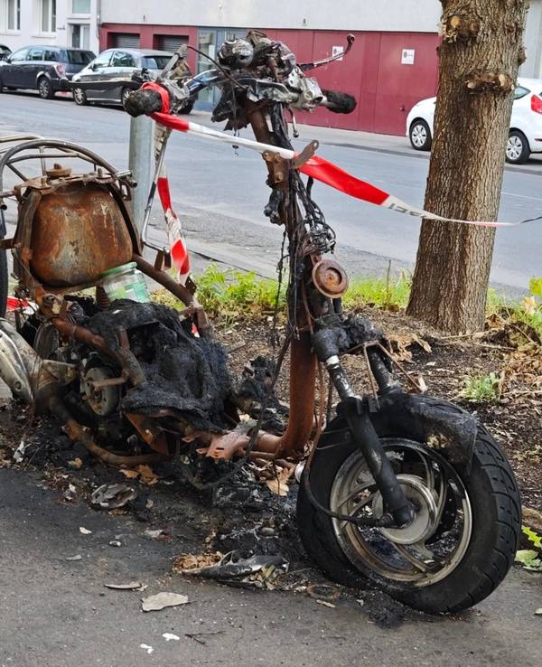 Ein ausgebranntes Zweirad-Wrack steht in Lindenthal an der Straße.