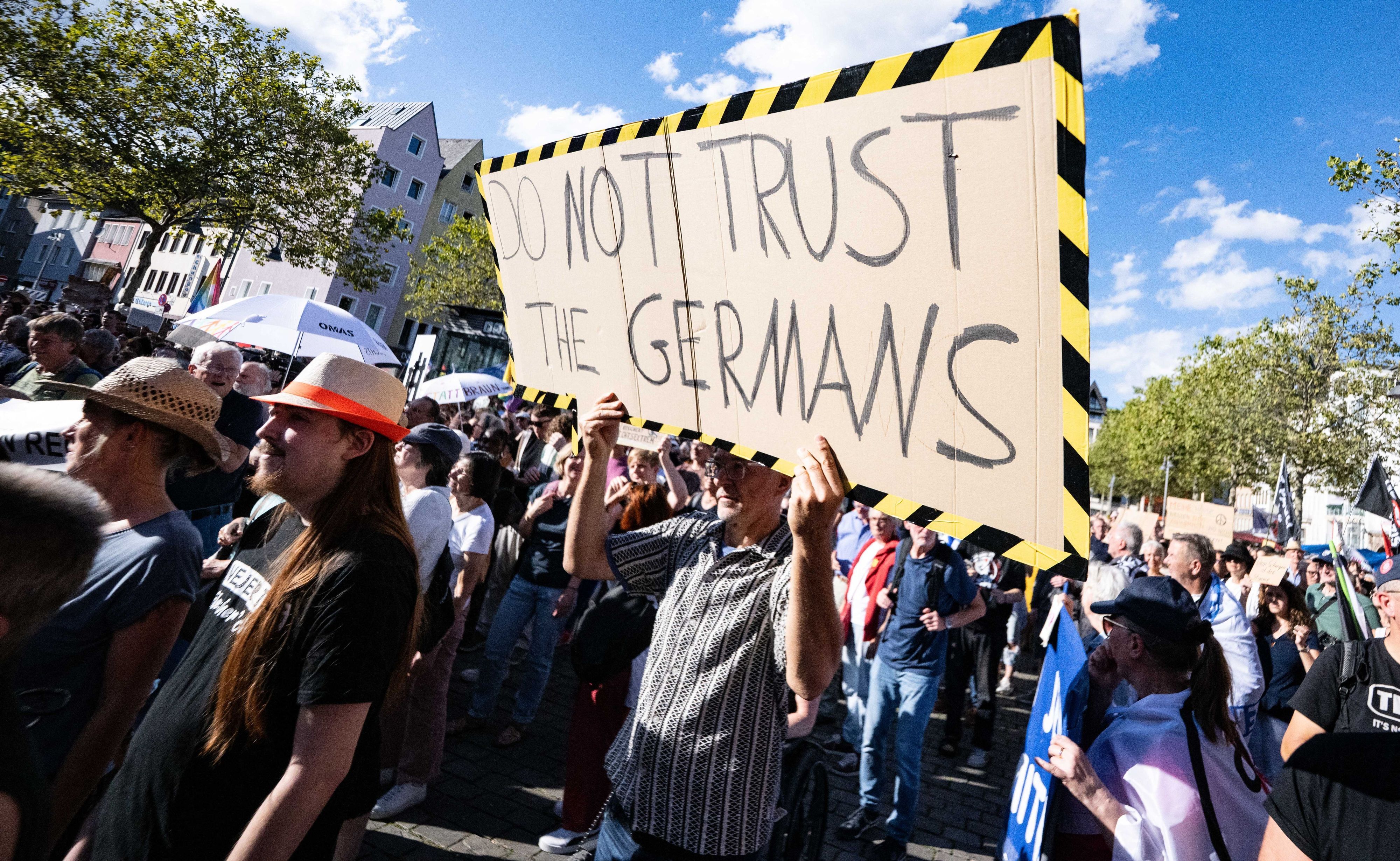Ein Demonstrant hält ein Schild mit der Aufschrift „Don't trust the Germans“ hoch.