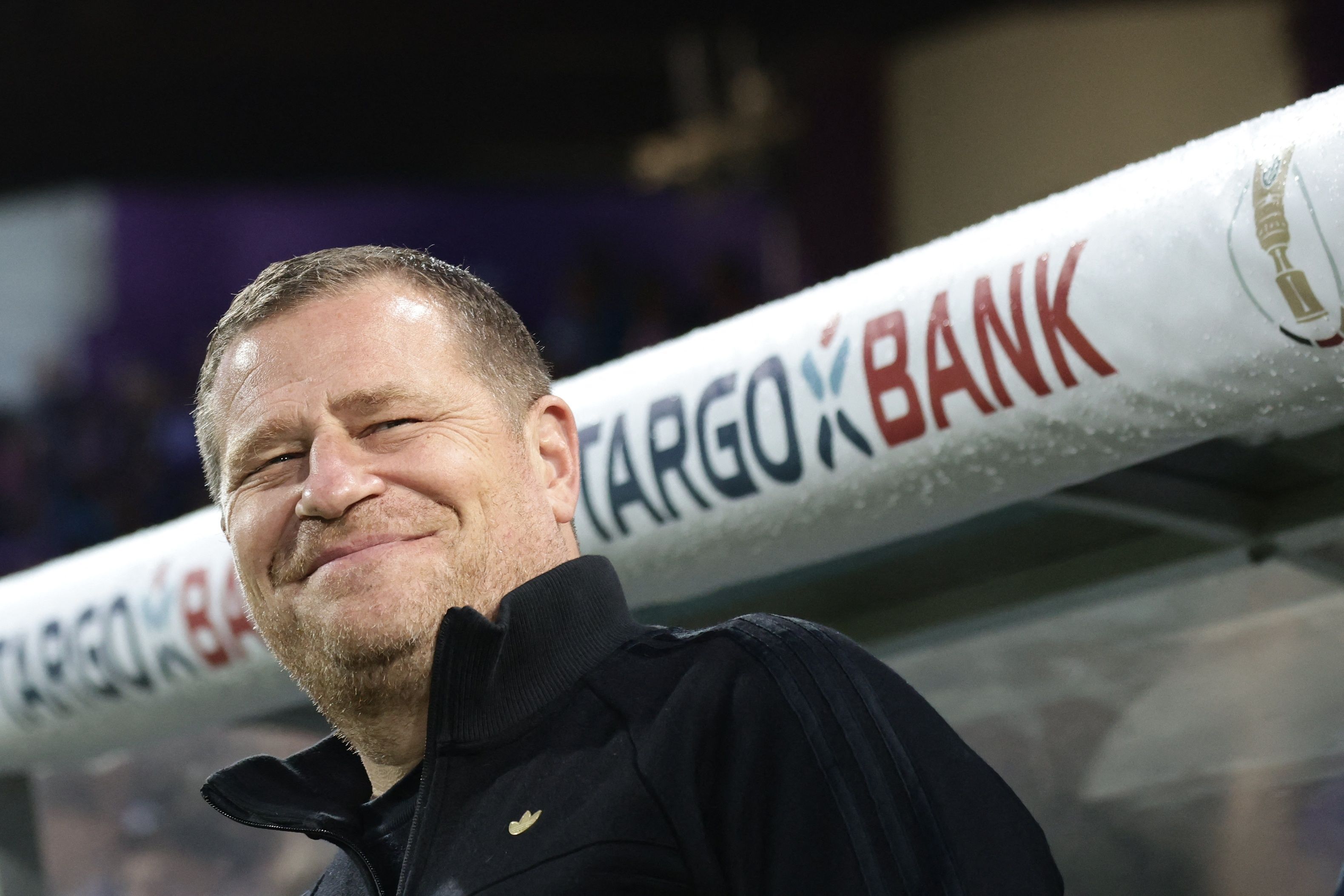 Max Eberl lächelt vor der Trainerbank.