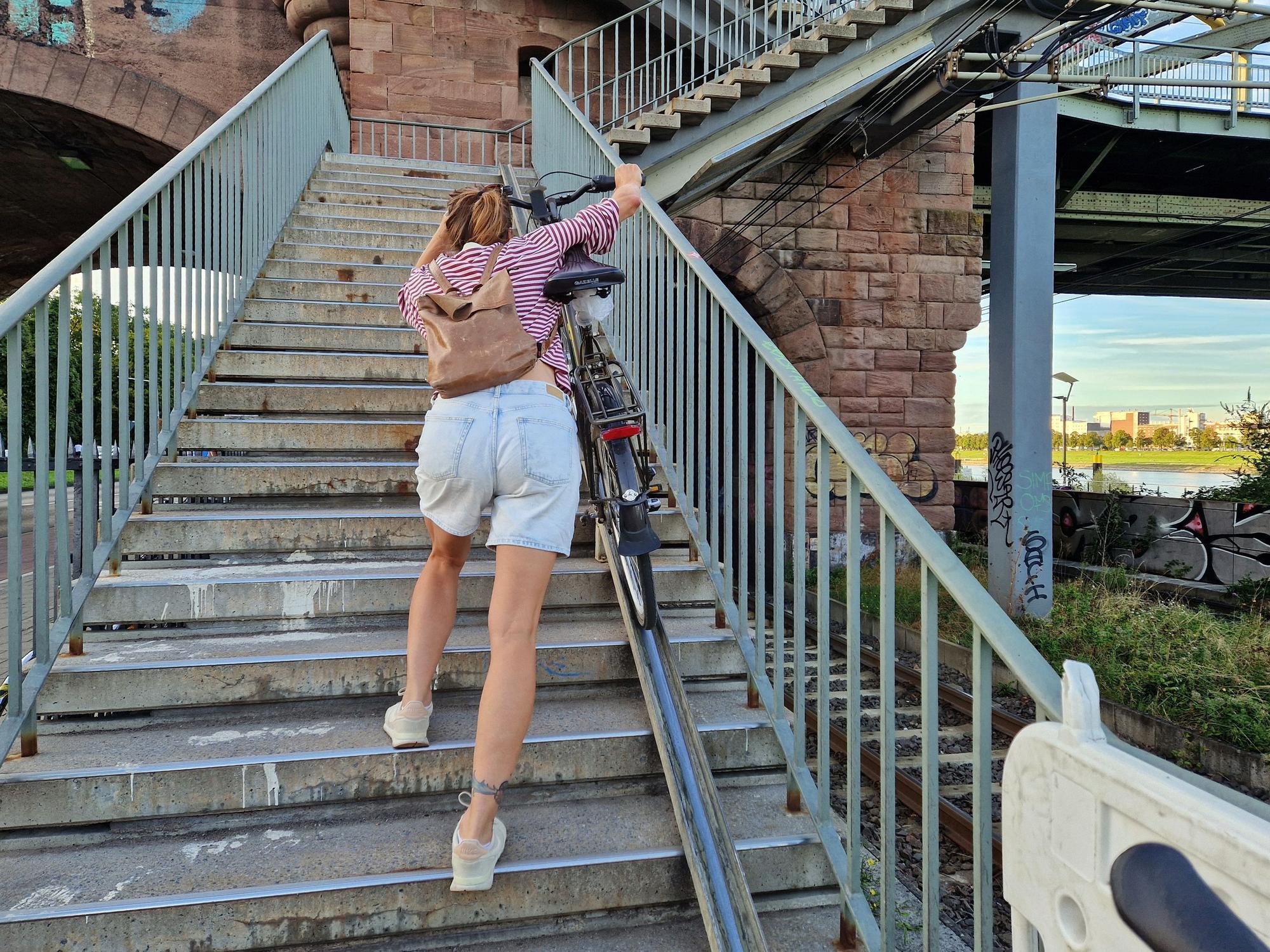 Eine Frau schiebt ihr Fahrrad über eine Schiene eine Treppe hoch.