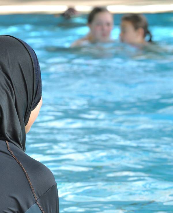 Eine muslimische Schülerin sitzt in einem Ganzkörperbadeanzug (Burkini) am Rande eines Schwimmbeckens.
