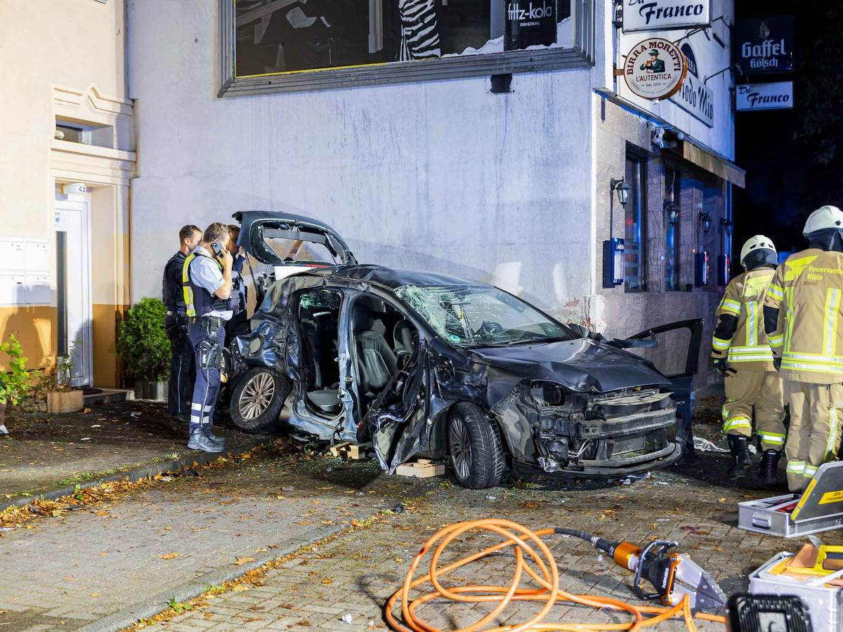 Ein völlig demolierter Pkw steht an einer Hauswand, Polizisten und Feuerwehrleute sind im Einsatz.