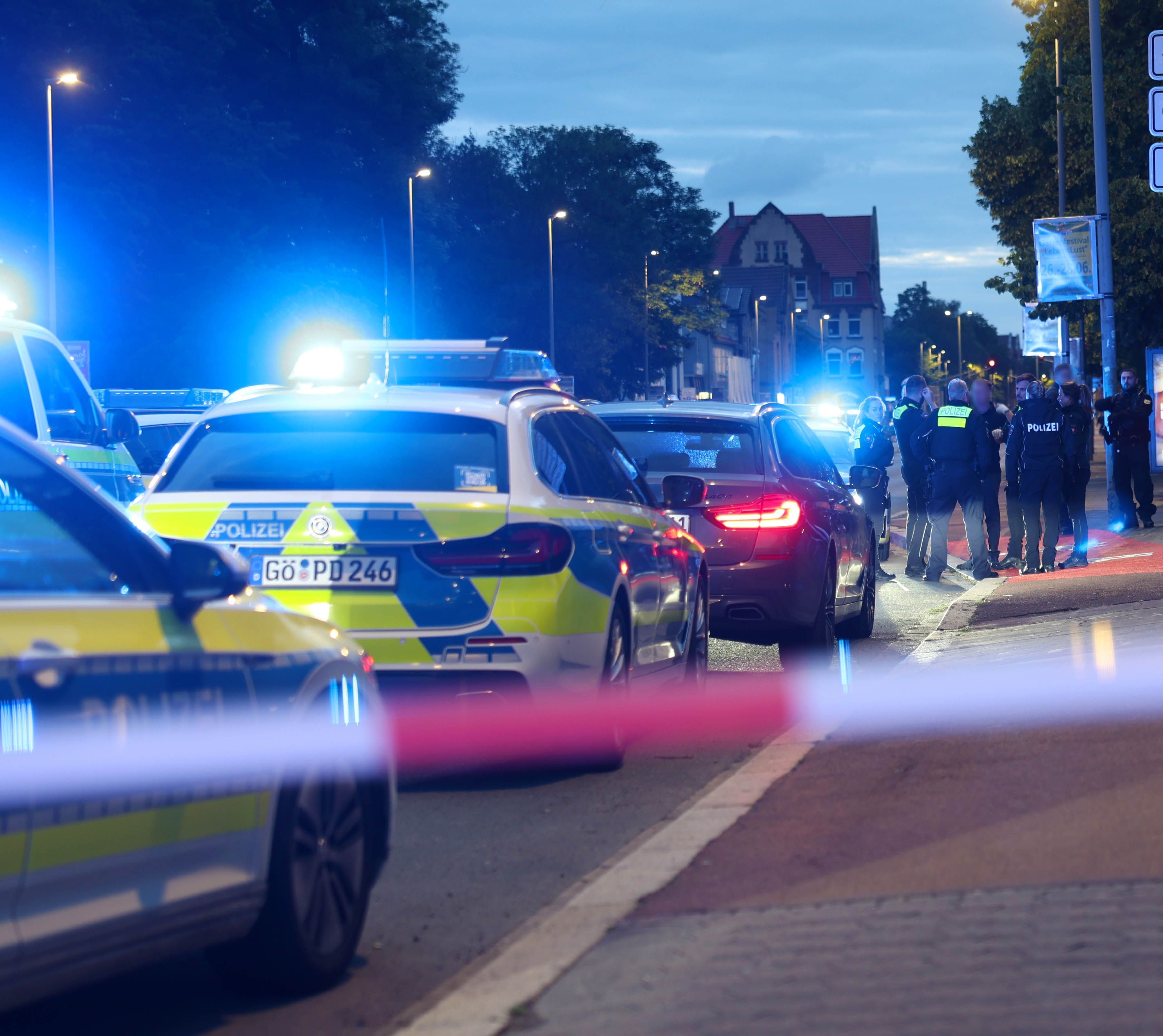 Polizisten und Polizeifahrzeuge stehen hinter einer Absperrung.