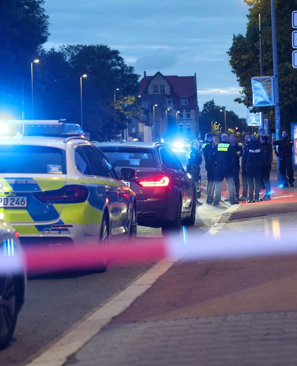 Polizisten und Polizeifahrzeuge stehen hinter einer Absperrung.