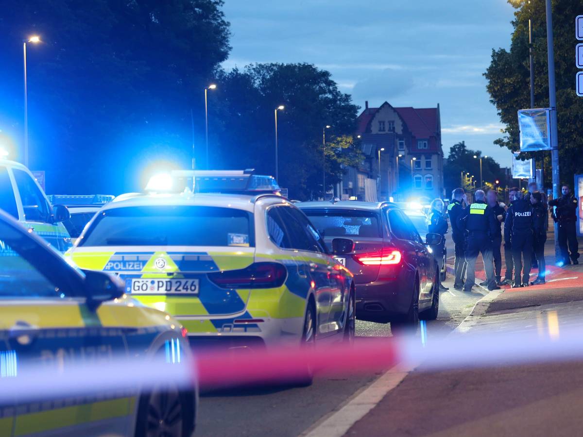 Polizisten und Polizeifahrzeuge stehen hinter einer Absperrung.