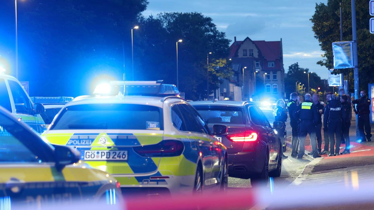 Polizisten und Polizeifahrzeuge stehen hinter einer Absperrung.