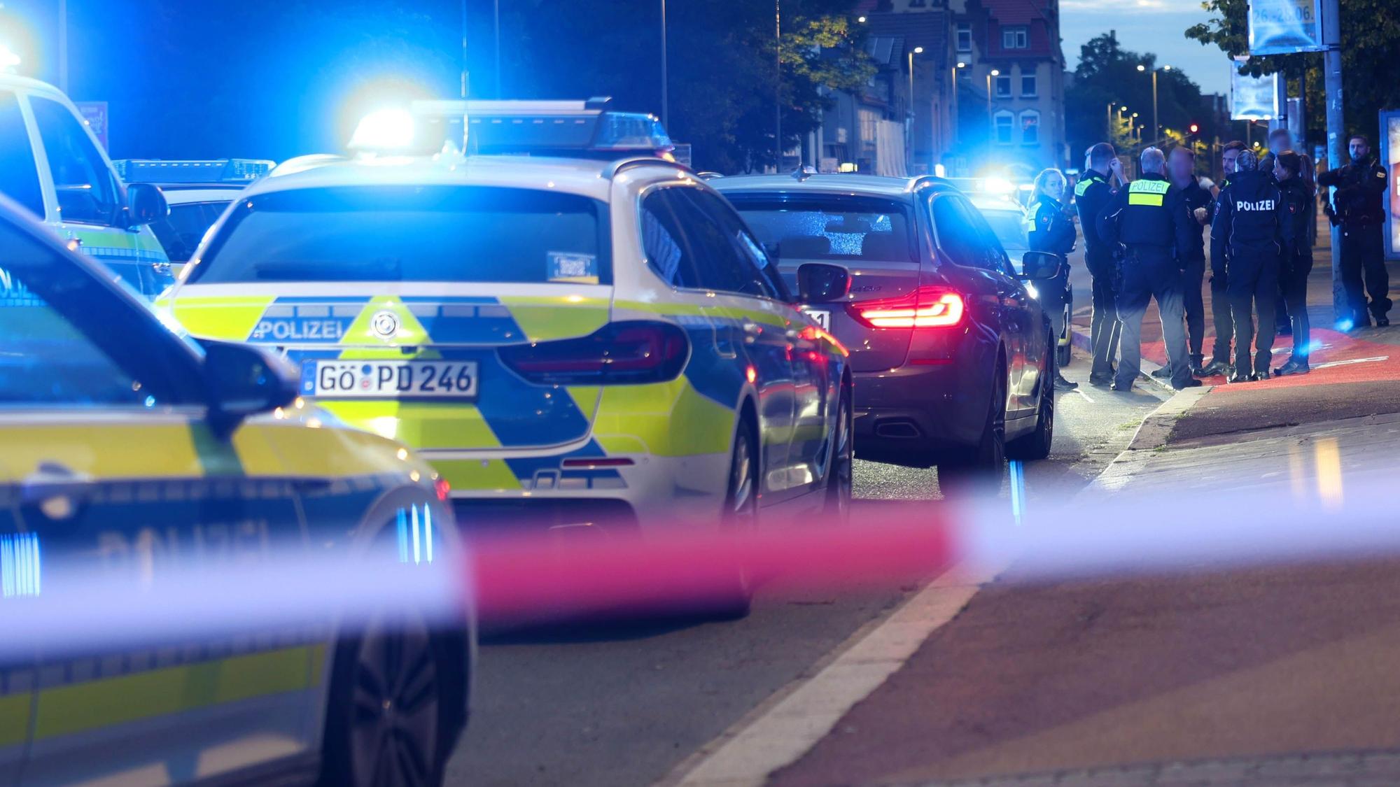 Polizisten und Polizeifahrzeuge stehen hinter einer Absperrung.