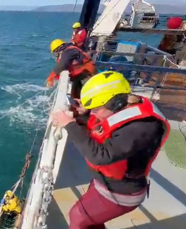 Ein Junge hockt auf einem gekenterten Boot und wird von einer Schiffsbesatzung gerettet.