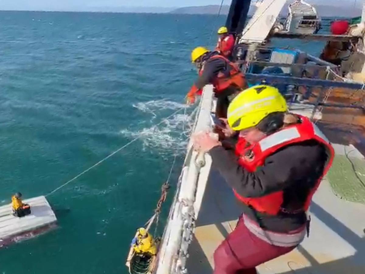 Ein Junge hockt auf einem gekenterten Boot und wird von einer Schiffsbesatzung gerettet.