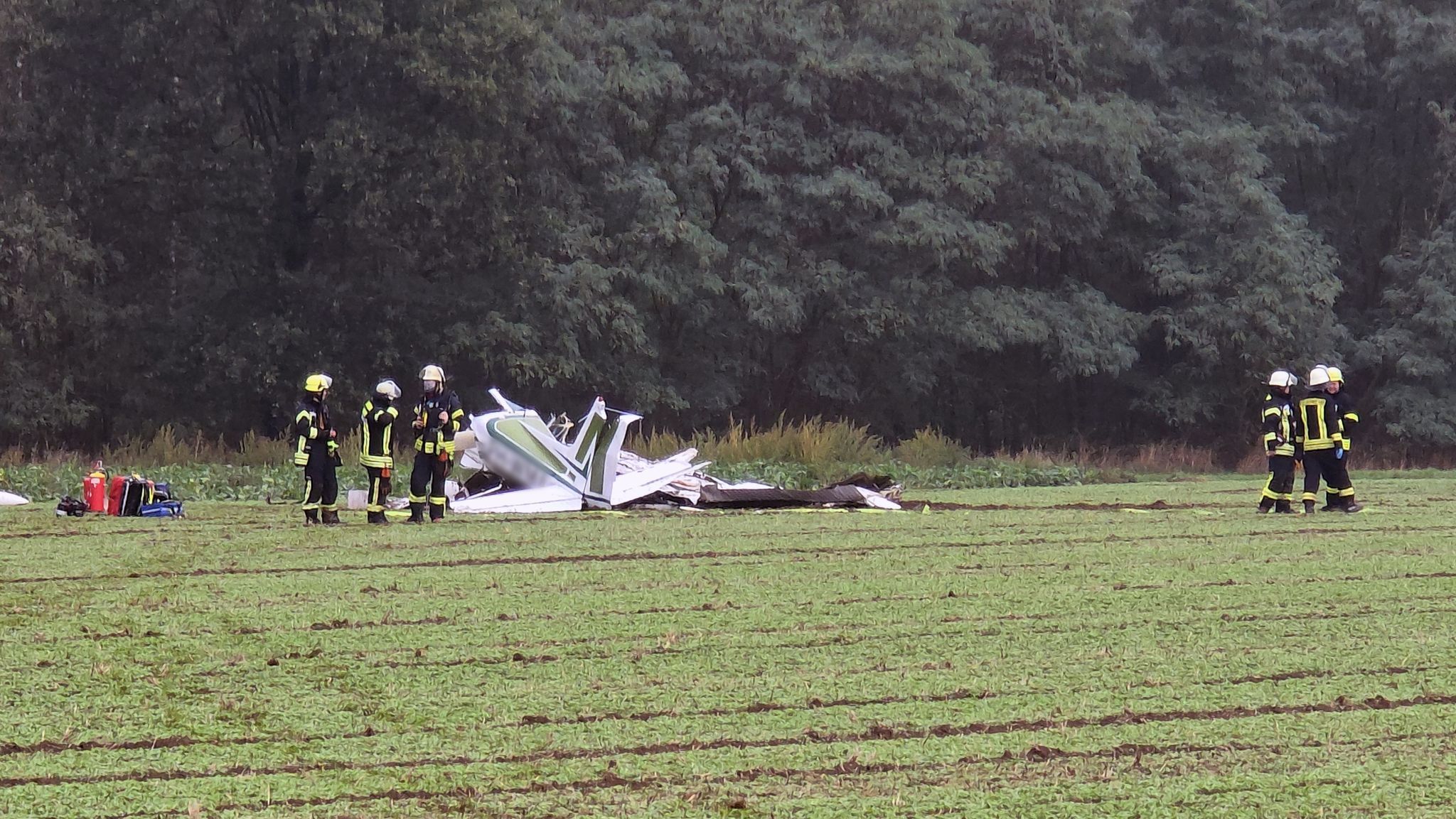 Ein zerschelltes Kleinflugzeug liegt auf einem Acker, Feuerwehrleute sind im Einsatz.