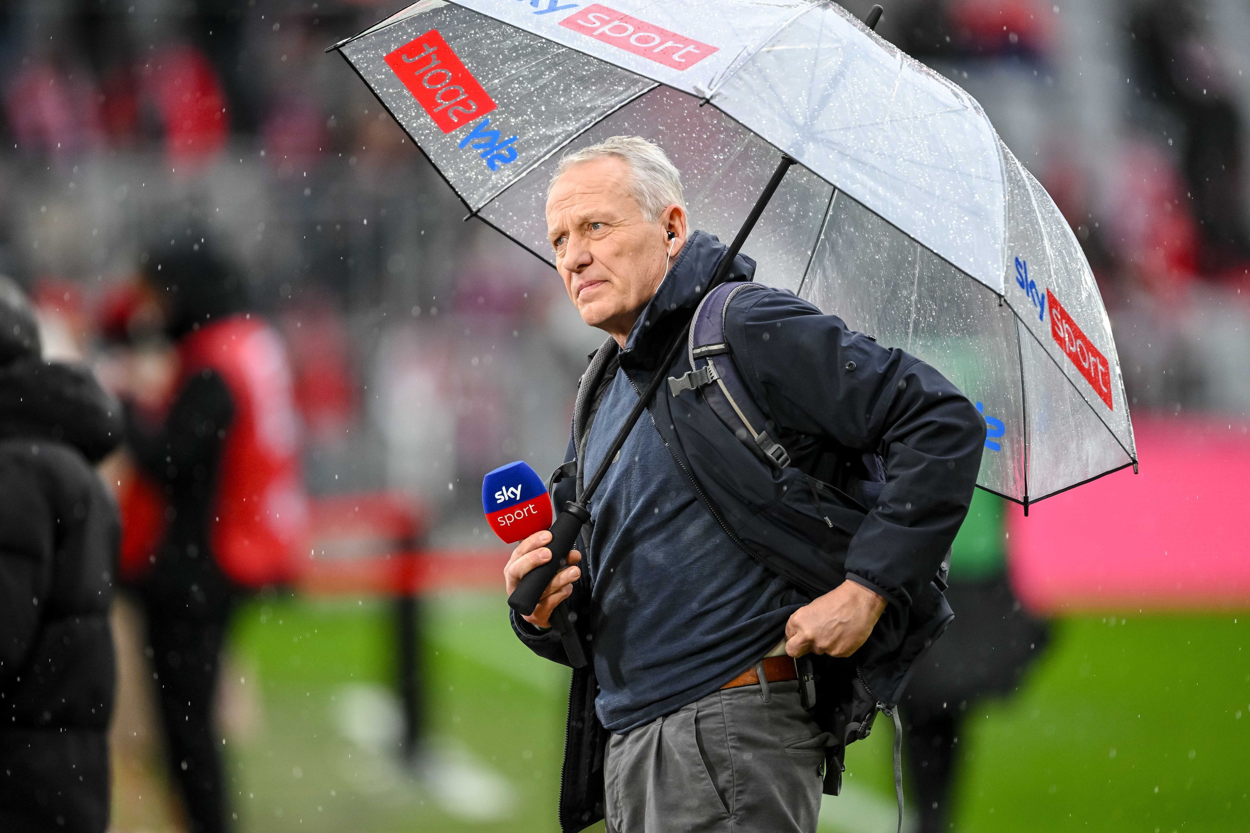 Christian Streich mit Mikrofon und Regenschirm