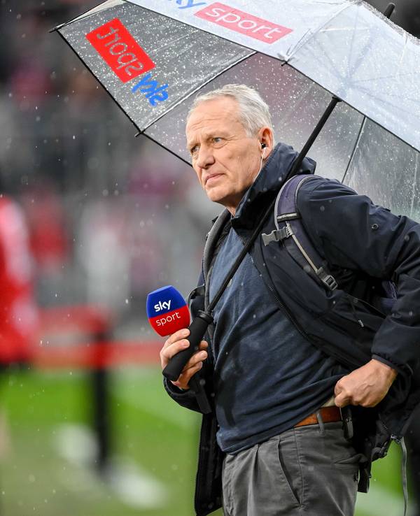 Christian Streich mit Mikrofon und Regenschirm