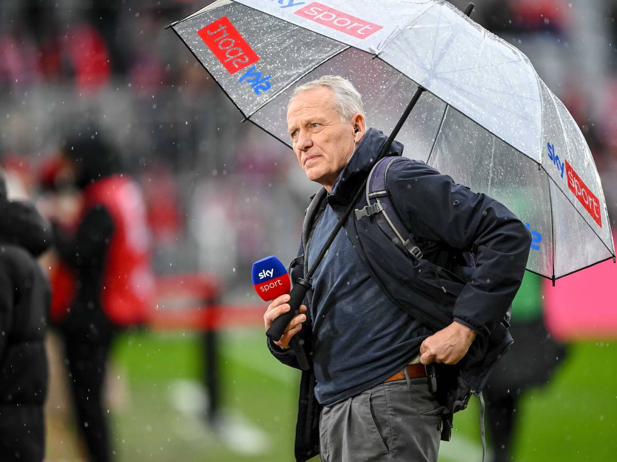 Christian Streich mit Mikrofon und Regenschirm