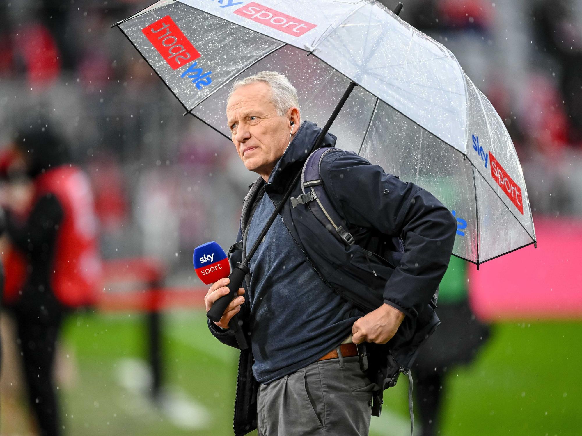 Christian Streich mit Mikrofon und Regenschirm
