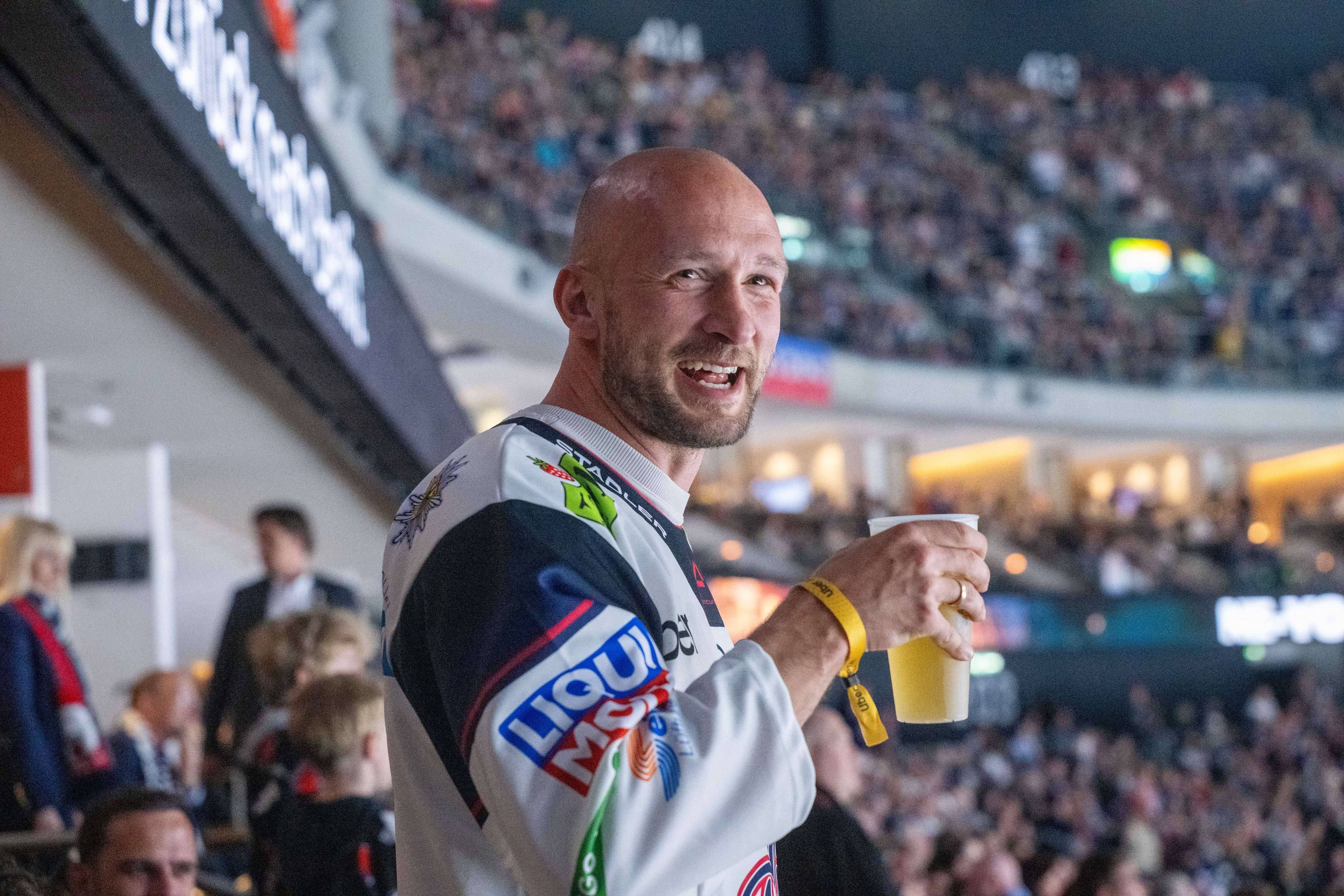 Toni Leistner mit Bierbecher in der Hand auf der Tribüne.