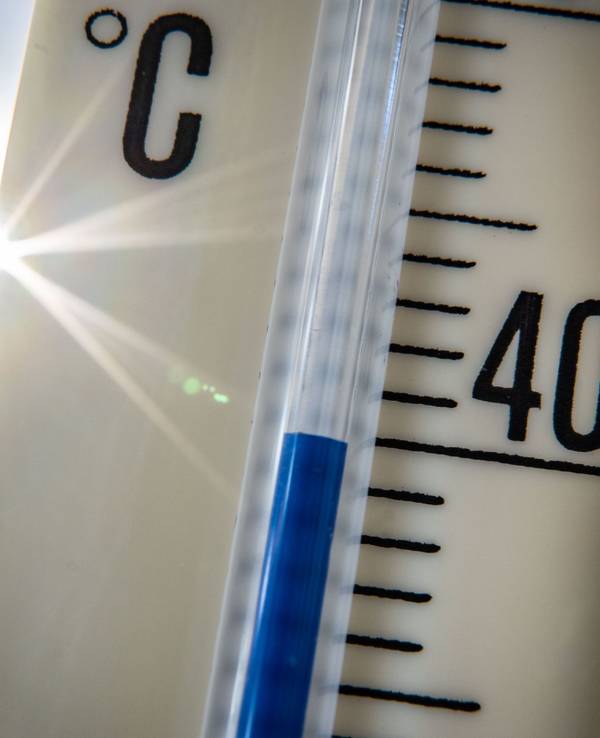 Ein Außenthermometer zeigt vor dem blauen Himmel und der Sonne eine Temperatur von nahezu 40 Grad Celsius an.