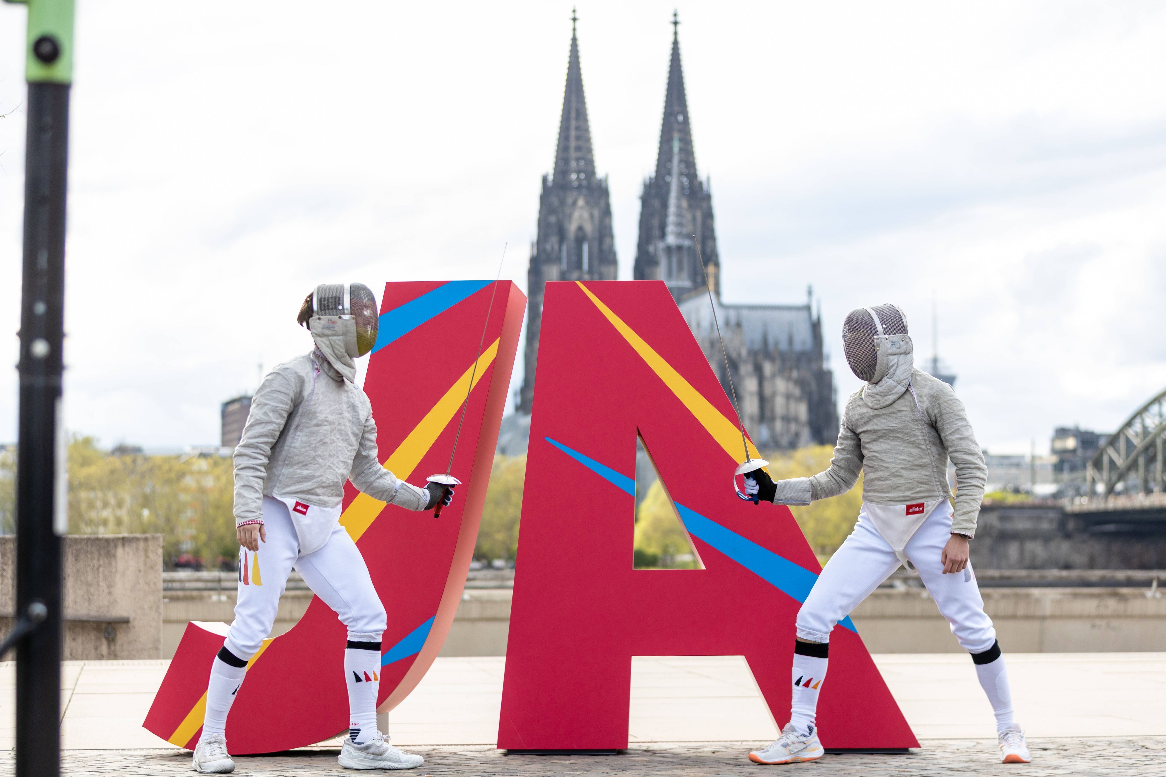 Zwei Fechter vor eine JA Logo vor dem Kölner Dom.
