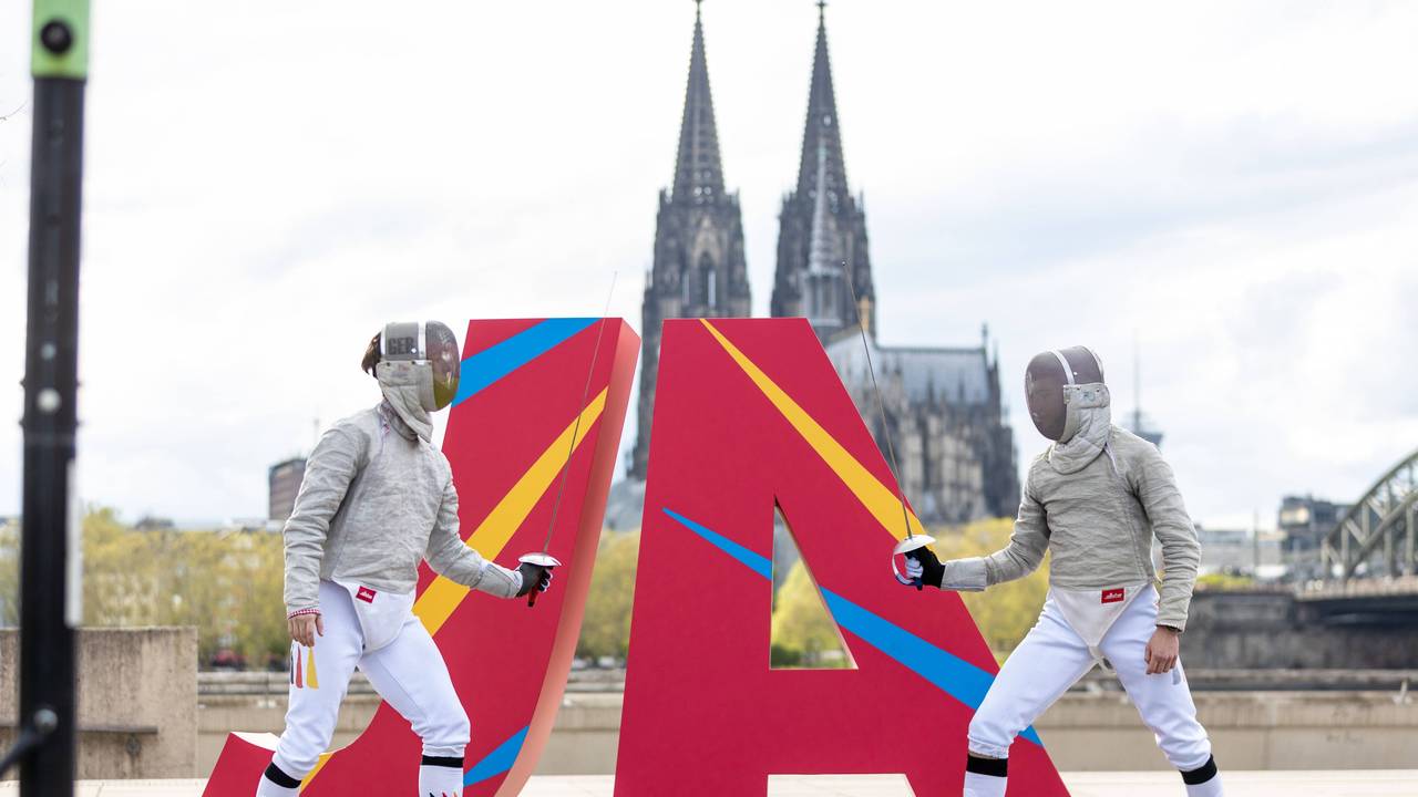 Zwei Fechter vor eine JA Logo vor dem Kölner Dom.
