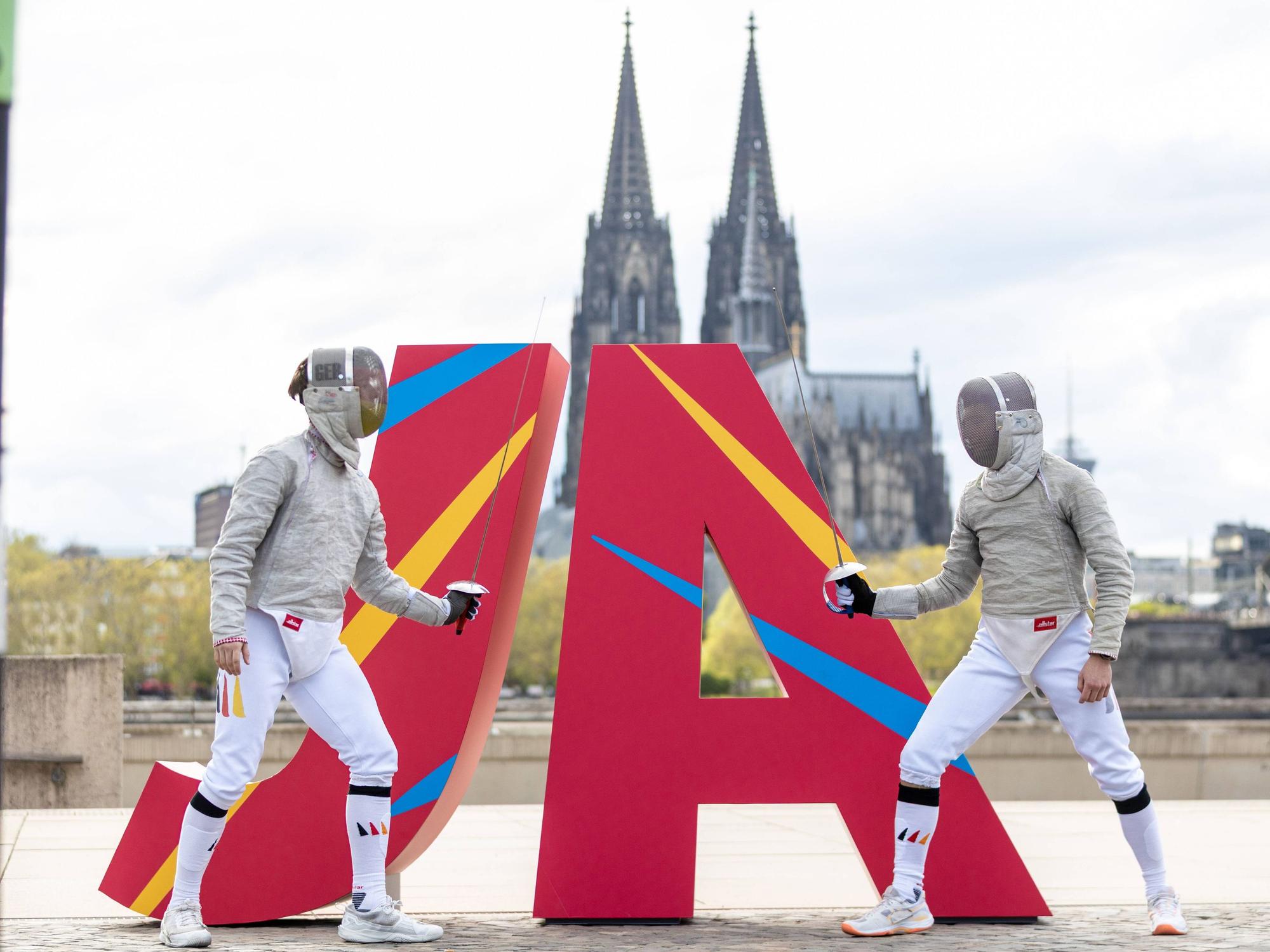 Zwei Fechter vor eine JA Logo vor dem Kölner Dom.