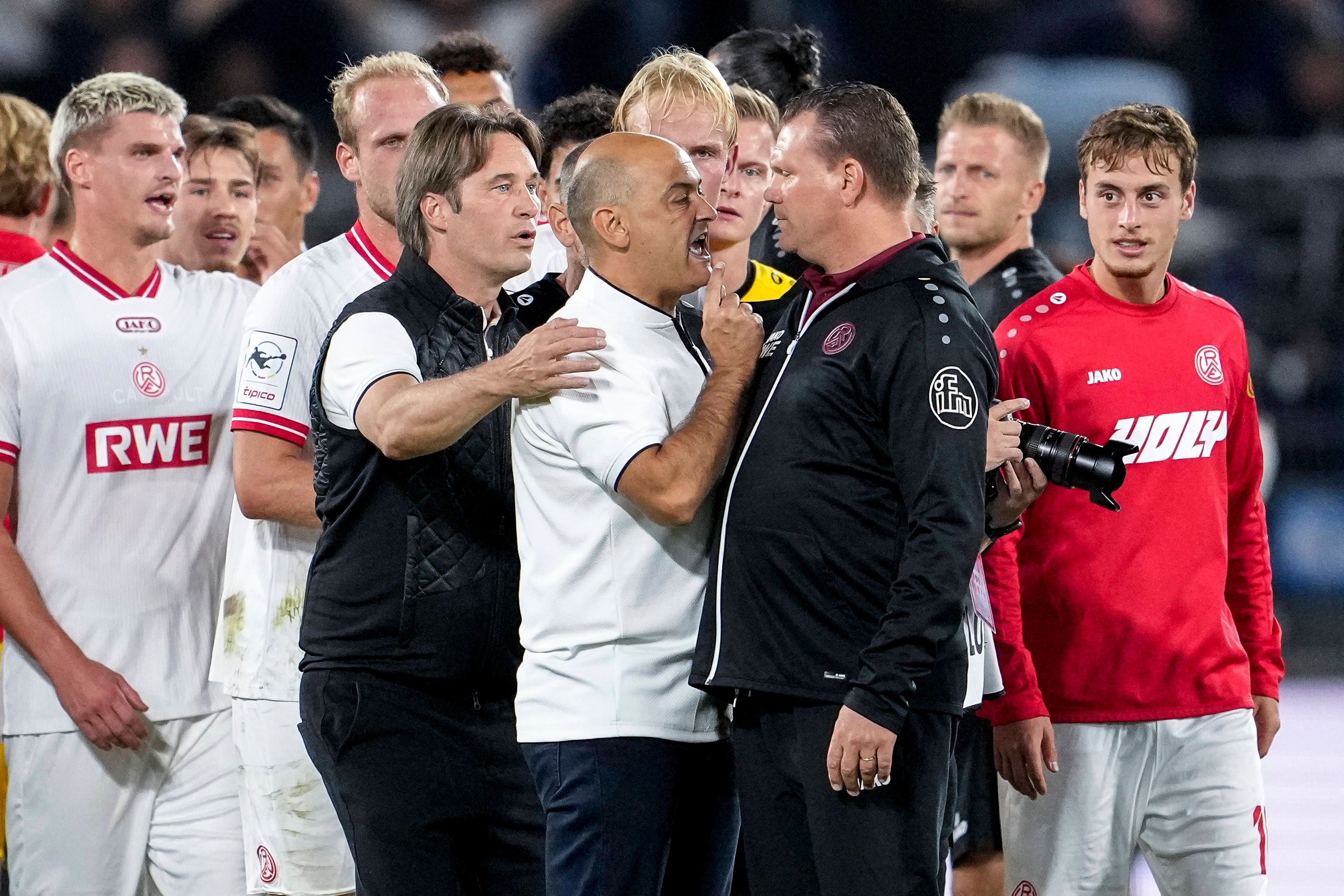 Gerhard Zuber hält Rui Mota zurück, der auf Uwe Koschinat einspricht.
