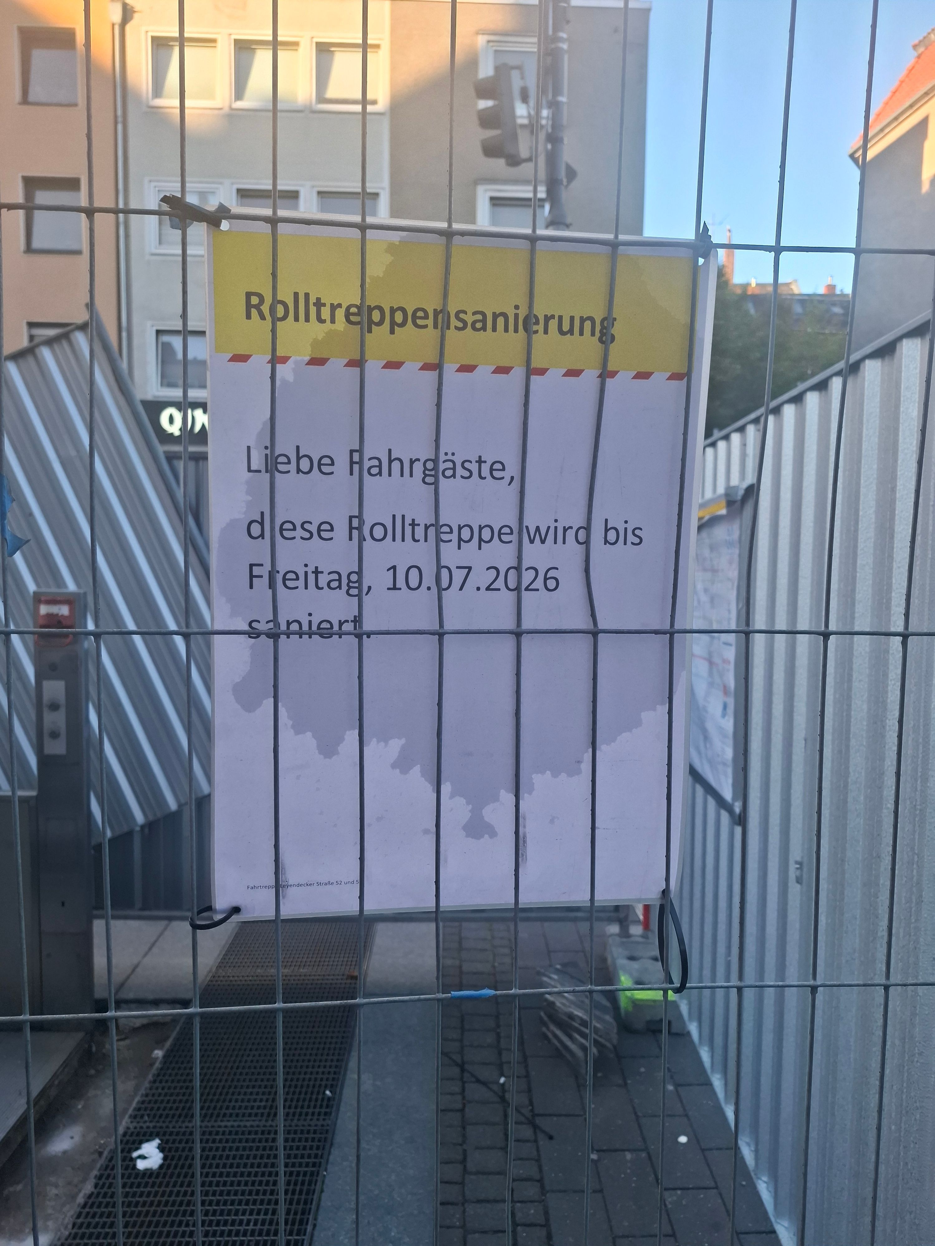 Der Bauzaun an der Haltestelle Piusstraße in Ehrenfeld. Laut Schild sollte die Rolltreppensanierung bereits abgeschlossen sein.