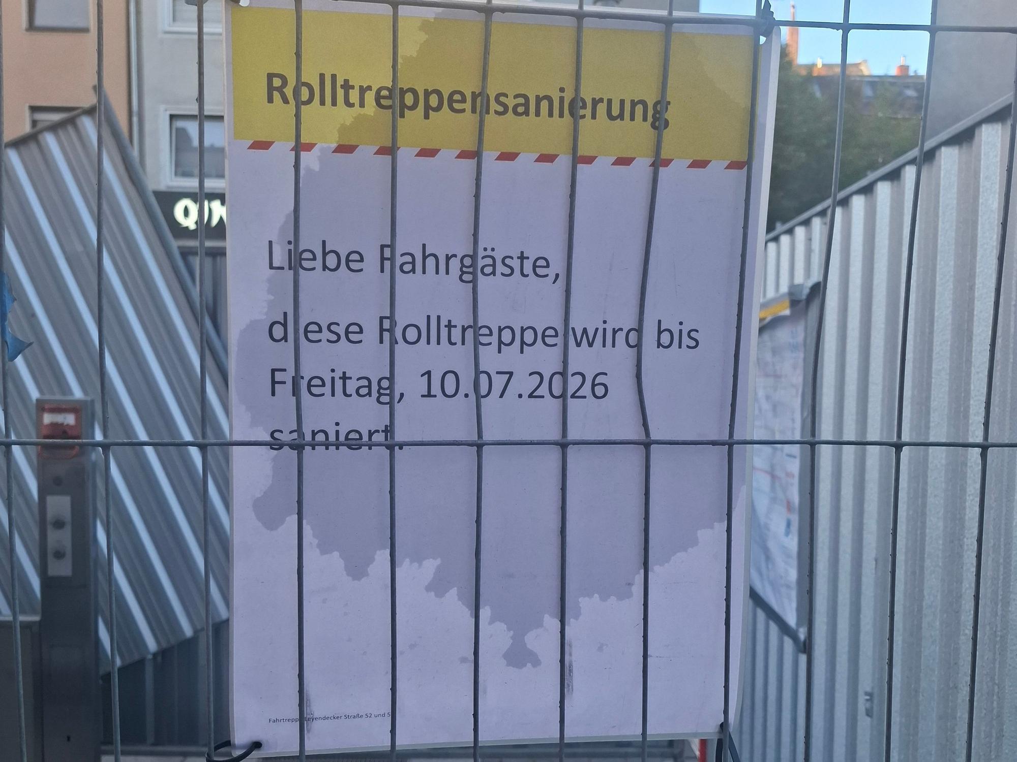 Der Bauzaun an der Haltestelle Piusstraße in Ehrenfeld. Laut Schild sollte die Rolltreppensanierung bereits abgeschlossen sein.