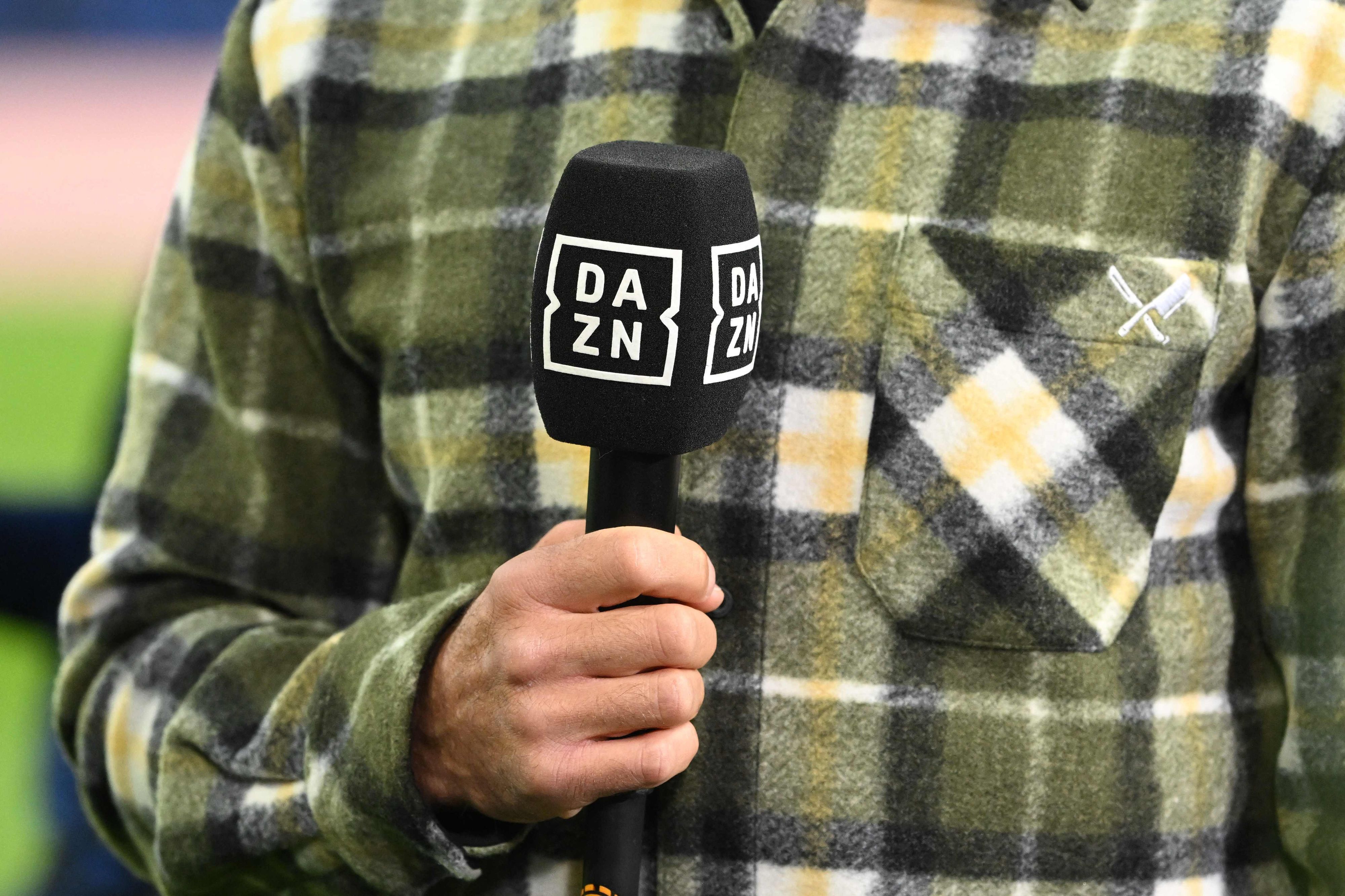 Ein Moderator hält am Rande eines Fußballspiels ein DAZN-Mikrofon in der Hand.