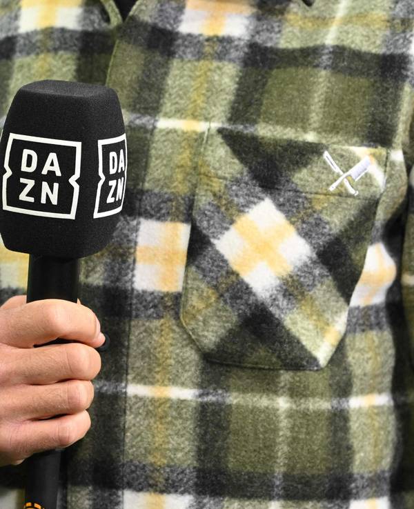 Ein Moderator hält am Rande eines Fußballspiels ein DAZN-Mikrofon in der Hand.