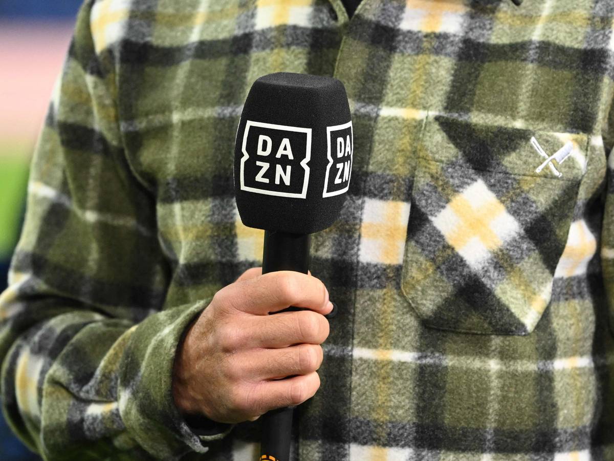 Ein Moderator hält am Rande eines Fußballspiels ein DAZN-Mikrofon in der Hand.