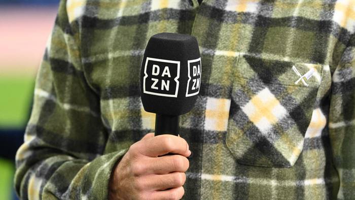 Ein Moderator hält am Rande eines Fußballspiels ein DAZN-Mikrofon in der Hand.