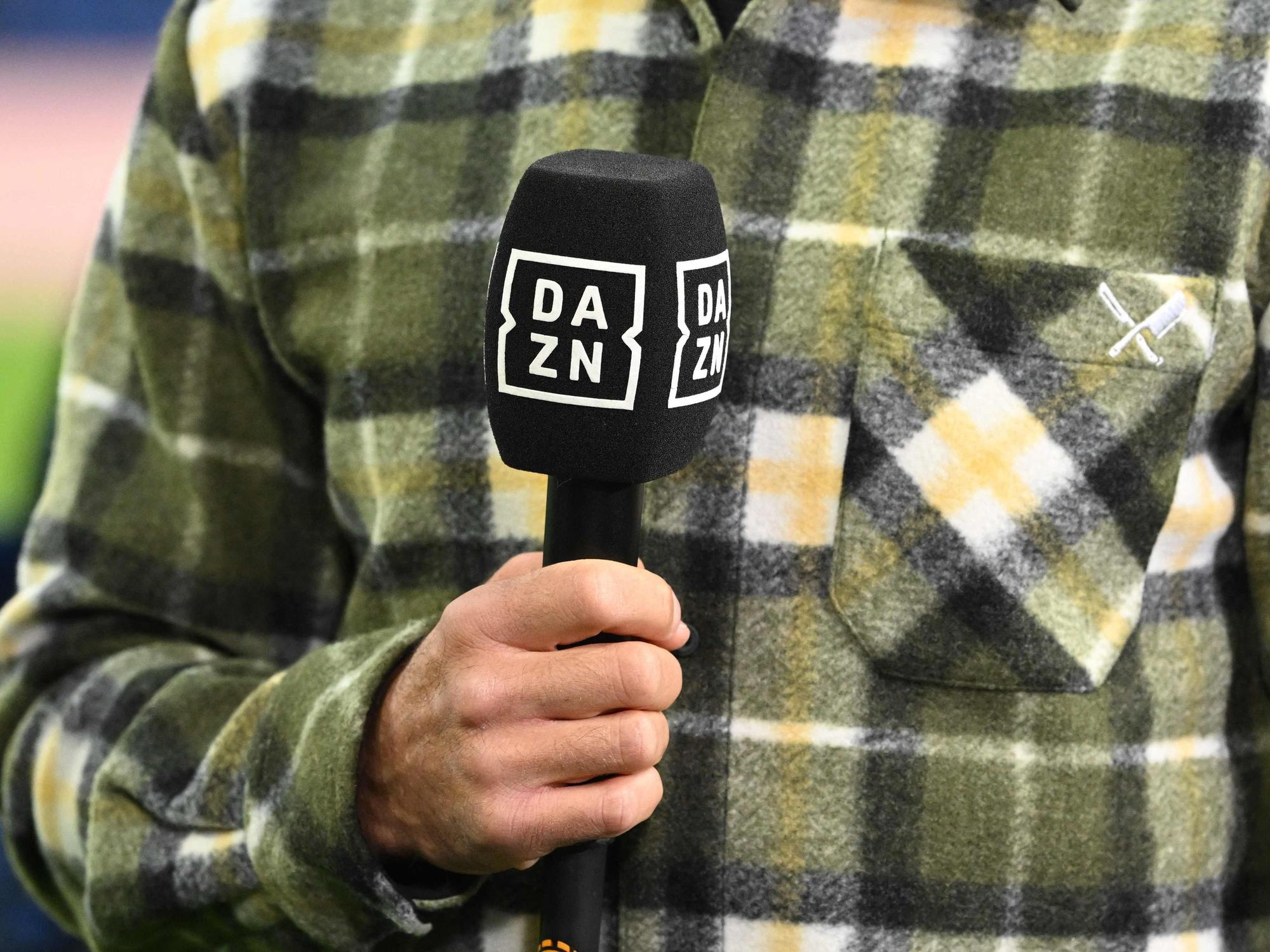 Ein Moderator hält am Rande eines Fußballspiels ein DAZN-Mikrofon in der Hand.
