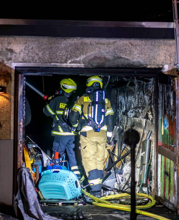 Zwei Feuerwehrleute stehen in der verrußten Garage, links ist im Vordergrund ein Feuerwehrmann von hinten unscharf zu sehen.