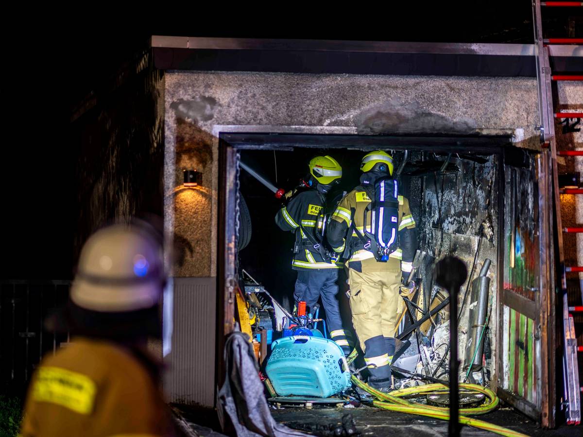 Zwei Feuerwehrleute stehen in der verrußten Garage, links ist im Vordergrund ein Feuerwehrmann von hinten unscharf zu sehen.