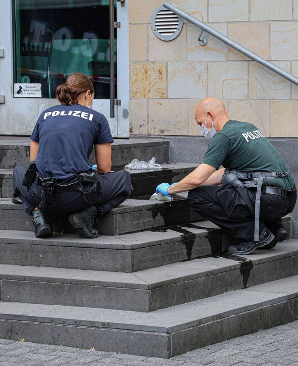 Eine Polizistin und ein Polizist hocken auf den Stufen der Synagoge und sichern Spuren.